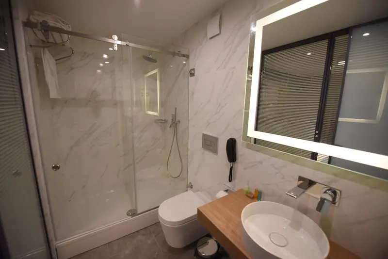 Mermer görünümlü banyo: cam duşakabin, aydınlatmalı ayna ve lavabo